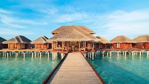 A wooden pier leading to overwater bungalows with thatched roofs.