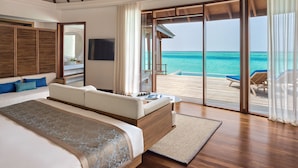 A spacious bedroom with a large bed, a television, and a view of the ocean through sliding glass doors.
