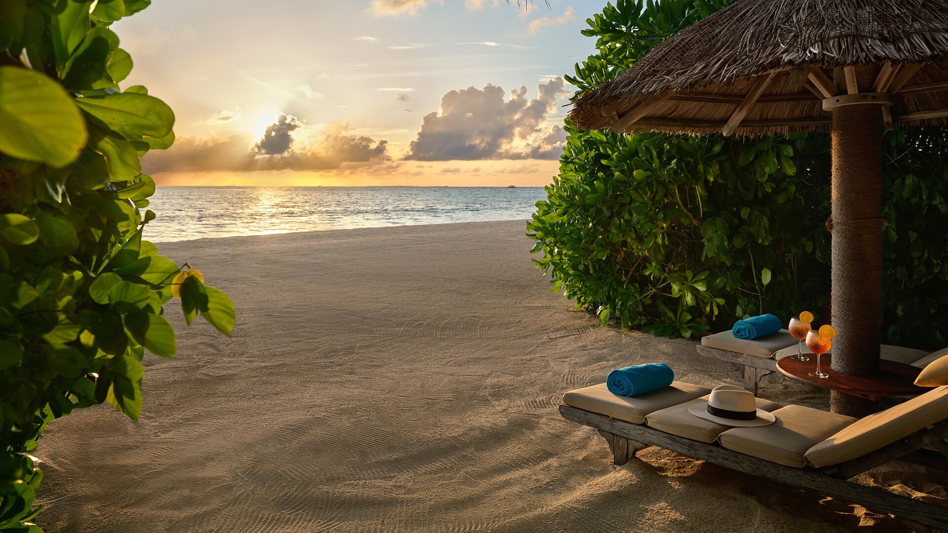 Un salón junto a la playa con techo de paja, sillones de descanso y vista al océano.