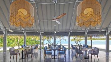 Un área de comedor al aire libre con mesas y sillas, un ventilador de techo y vistas al mar.