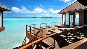 A wooden deck with lounge chairs and a view of a turquoise sea and an island.