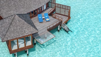 An overwater bungalow with a thatched roof, wooden deck, and two lounge chairs.
