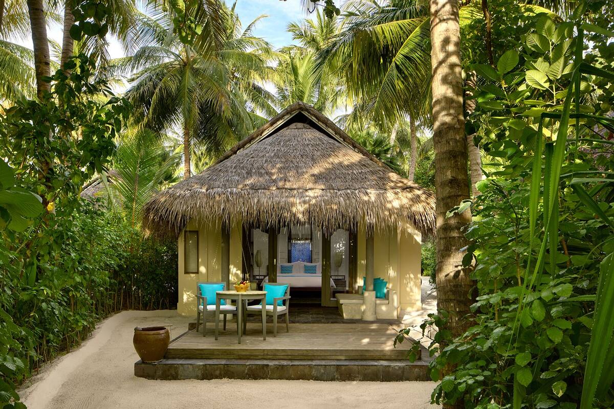 A thatched-roof hut with a wooden deck, a table, and chairs.
