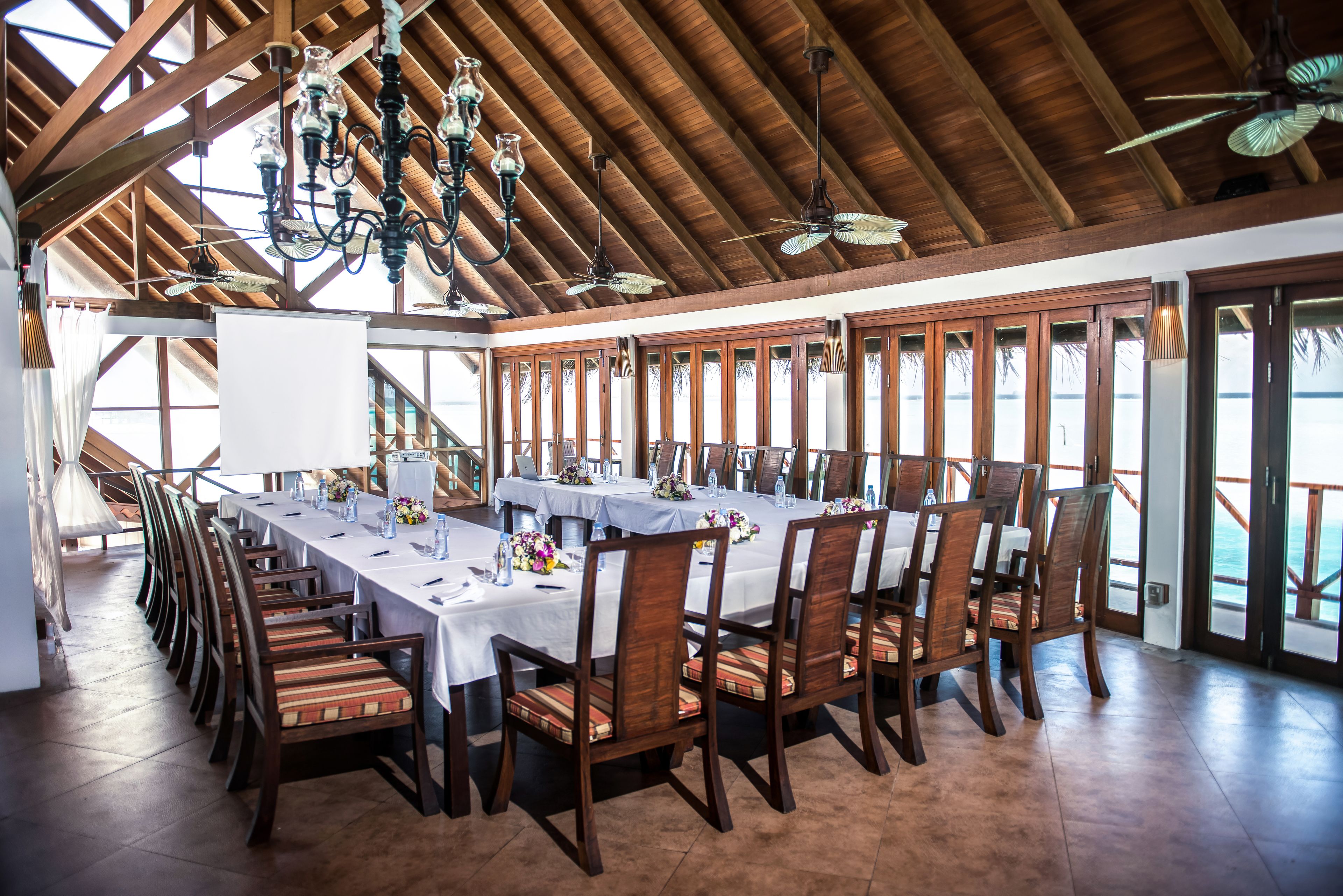 Un amplio comedor con mesas largas, sillas de madera y un techo alto con vigas a la vista y candelabros.