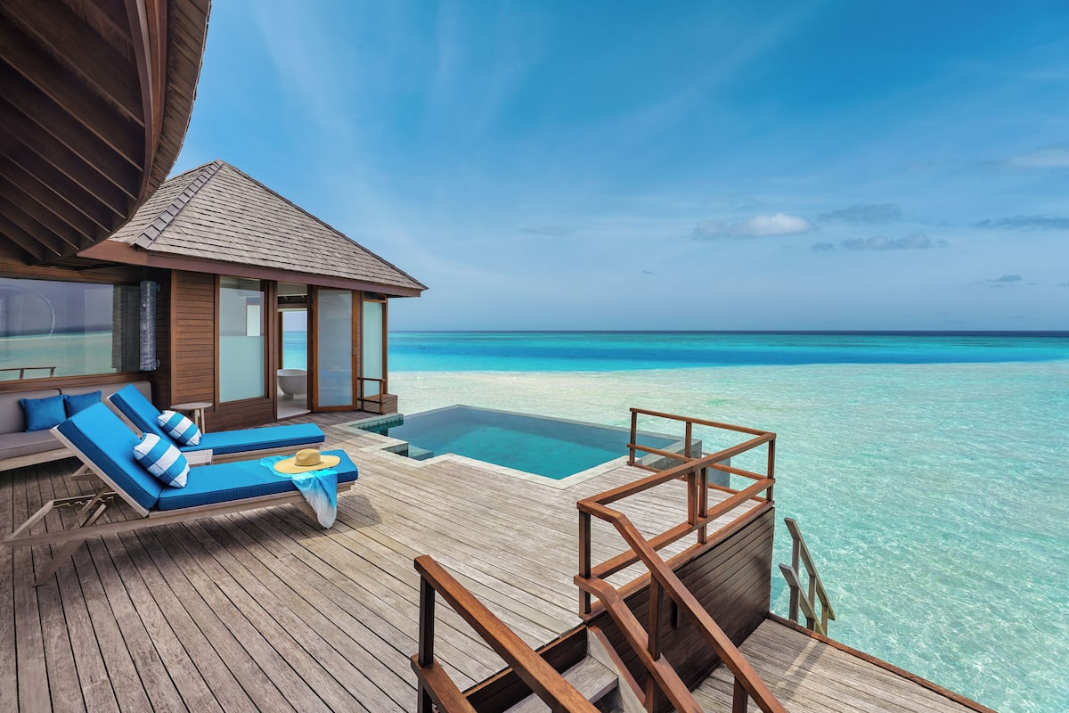 An overwater bungalows with wooden deck, infinity pool, and ocean views.
