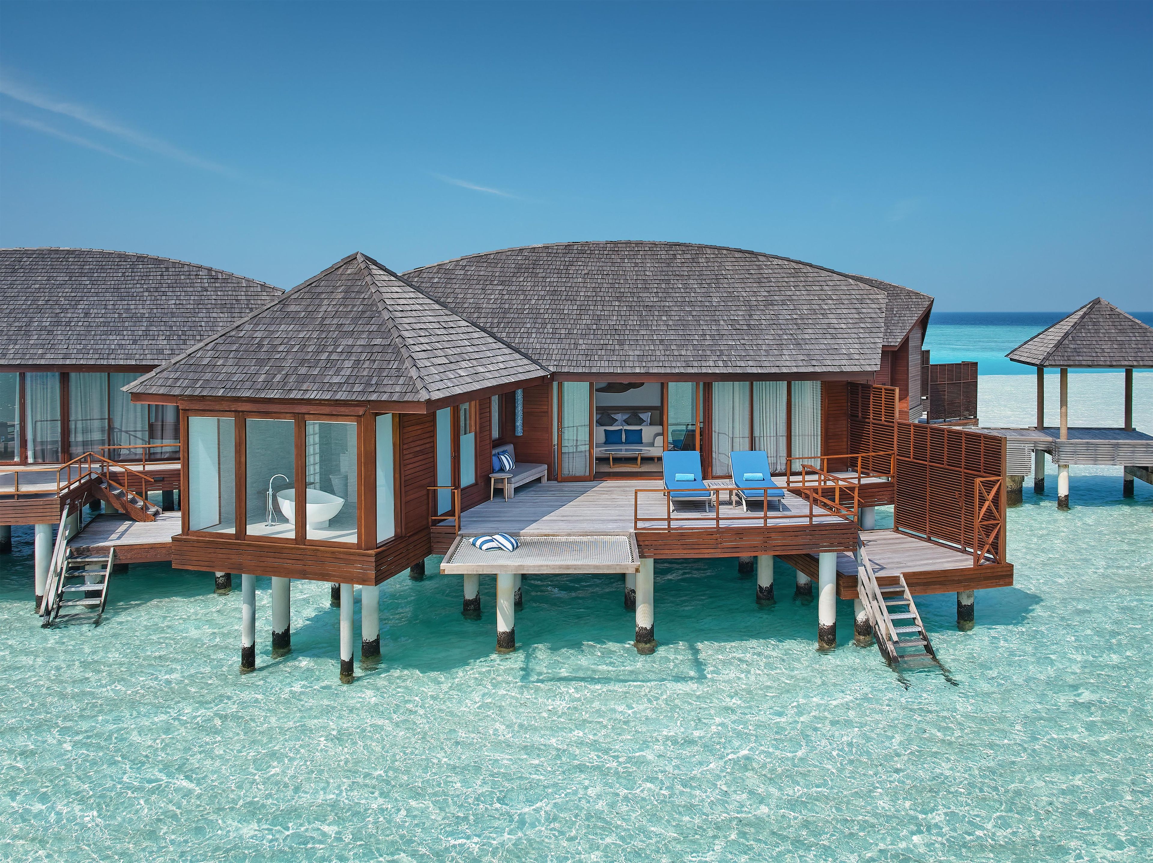 Bungalow sull'acqua con ponti in legno, acque cristalline e poltrone relax.