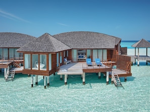 Overwater bungalows with wooden decks, clear blue water, and lounge chairs.