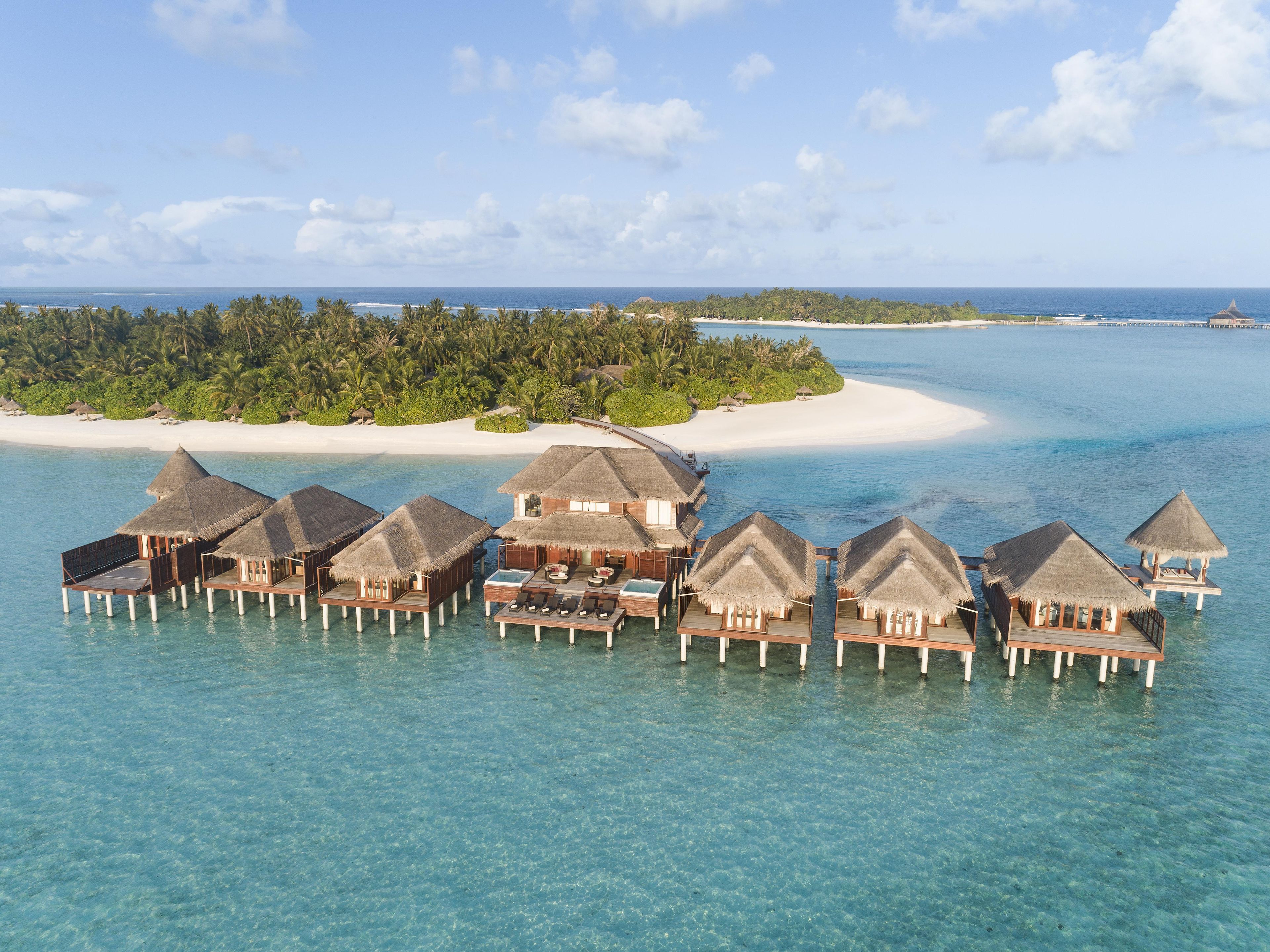 Bungalows sobre el agua con techos de paja, construidos sobre pilotes, sobre aguas turquesas cristalinas, rodeados por una isla tropical.