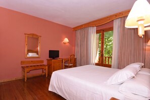 A bedroom with a bed, a desk, a chair, a television, and a window with curtains.