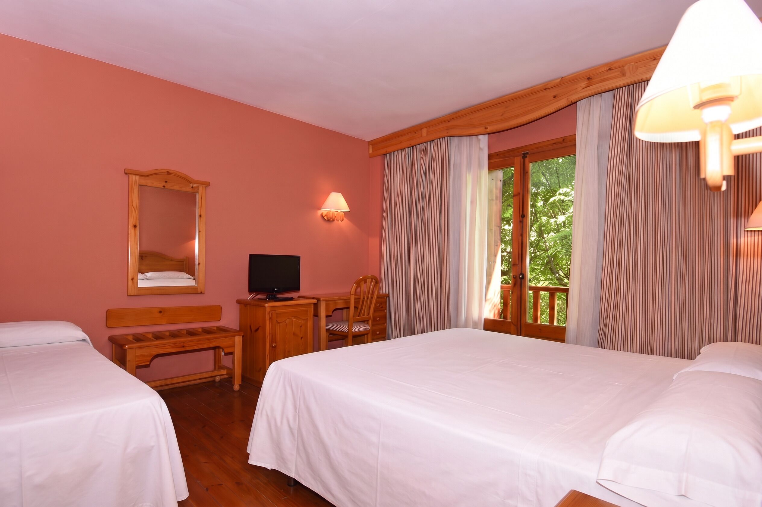 A hotel room with two beds, a desk, a television, and a window with curtains.