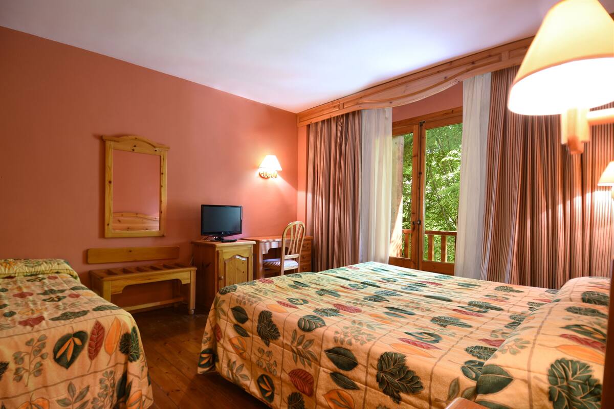 Habitación de hotel con dos camas, un escritorio, televisión y ventana con cortinas.