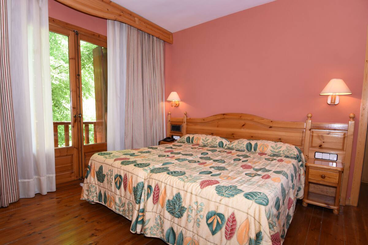 Un dormitorio con una cama de madera, una mesita de noche, una lámpara y una ventana con cortinas.