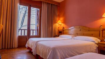 Habitació d'hotel amb dos llits, ambres de fusta, una tauleta de nit amb una làmpada i una finestra gran amb cortines.
