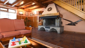 Una sala de estar acogedora con techo de madera, chimenea de piedra, sofá rojo y mesa de centro de madera con un juego de mesa.
