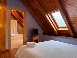 A bedroom with a sloped ceiling, a flat-screen TV, a bed with a white comforter, and a window. -  RVHotels Orri (Naut Aran)