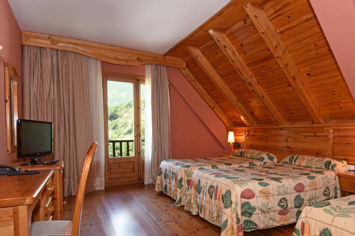 Un dormitorio acogedor con vigas de madera, un escritorio con computadora y dos camas con ropa de cama floral.