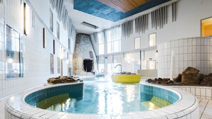 A large indoor swimming pool with a stone wall and a waterfall feature. - Lapland Hotels Luostotunturi (Sodankyla)