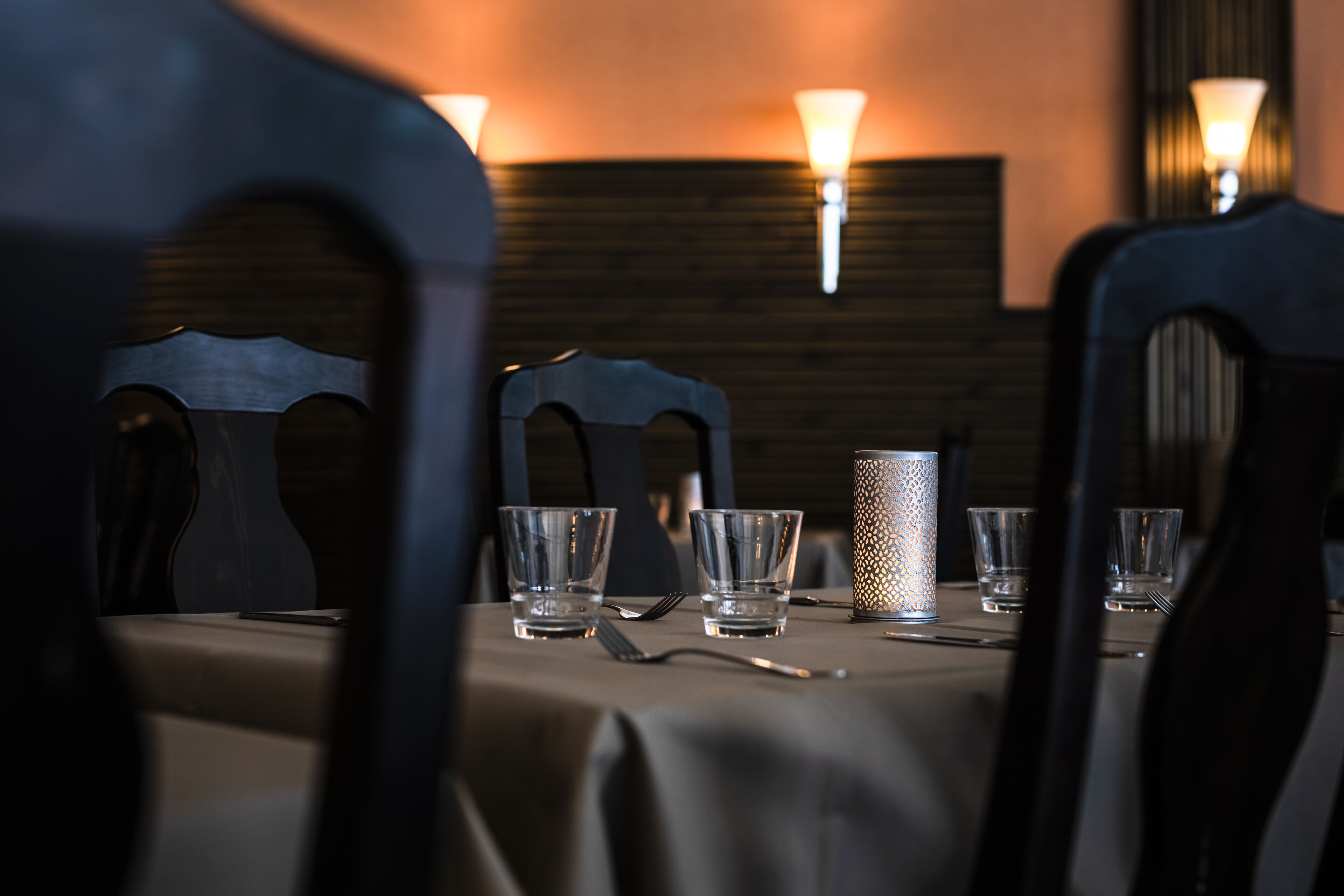 A table set for dining with chairs, glasses, cutlery, and a candle.