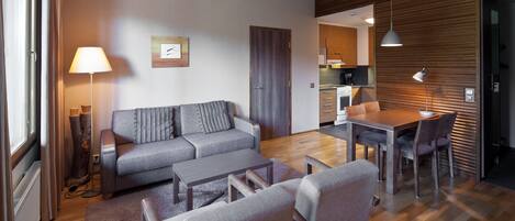 A modern living room with a sofa, coffee table, and chairs, a dining area with a table and chairs, and a kitchen in the background.