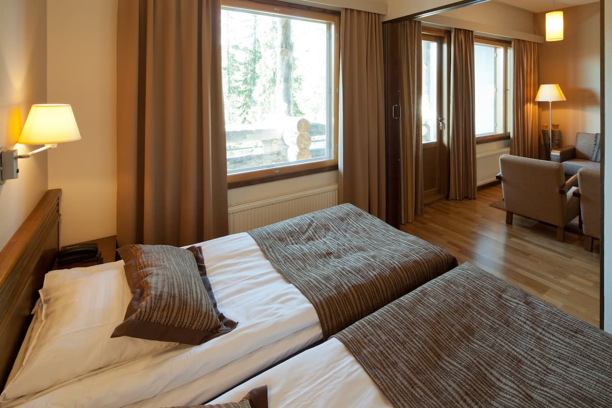 Habitación de hotel con cama, dos mesitas de noche, una silla, una lámpara y vistas al exterior.