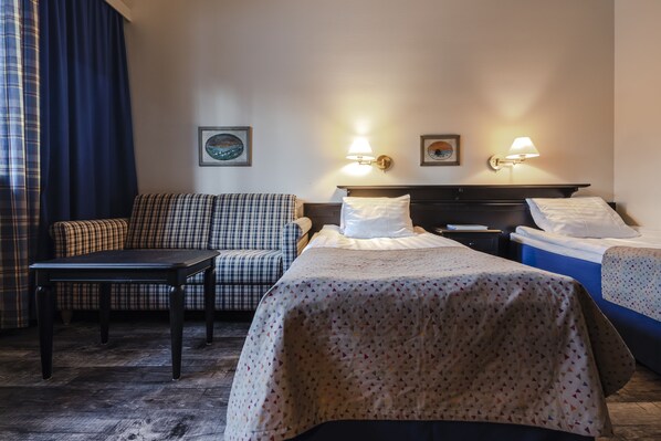 Habitación de hotel con sofá, dos camas, una mesita de noche y lámparas de pared.