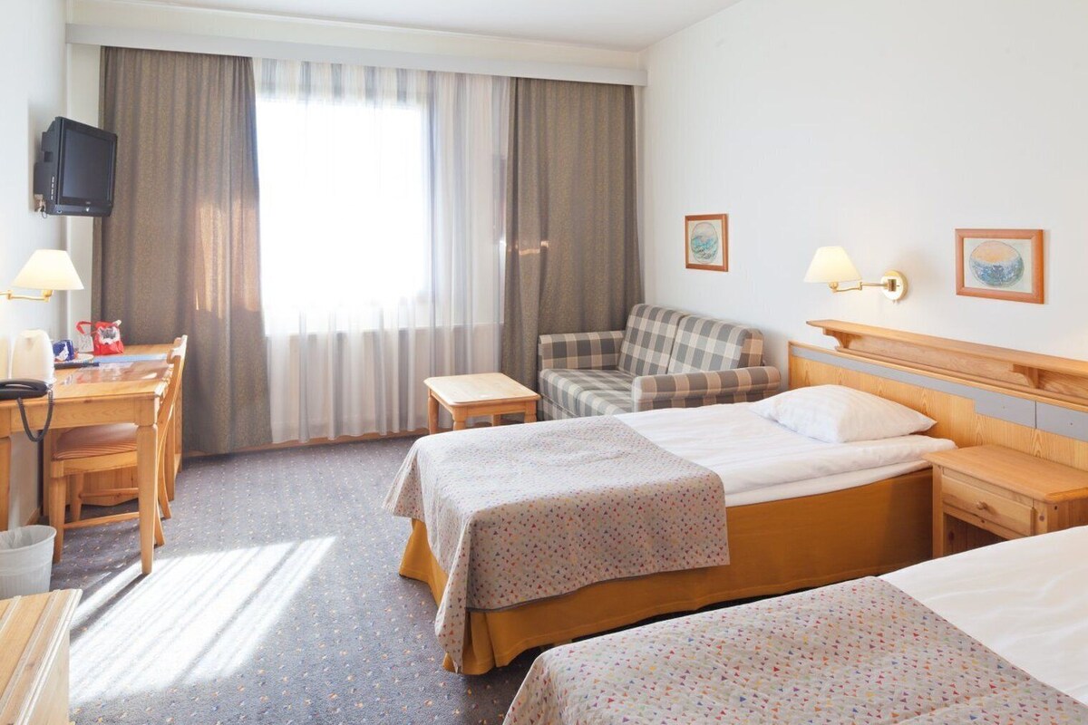 A hotel room with two beds, a desk, a chair, a television, and a window with curtains.