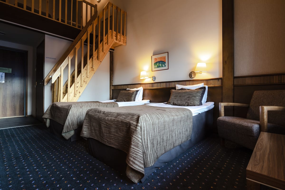 Una habitación de hotel con dos camas, una escalera de madera, una lámpara de pared y una alfombra estampada.