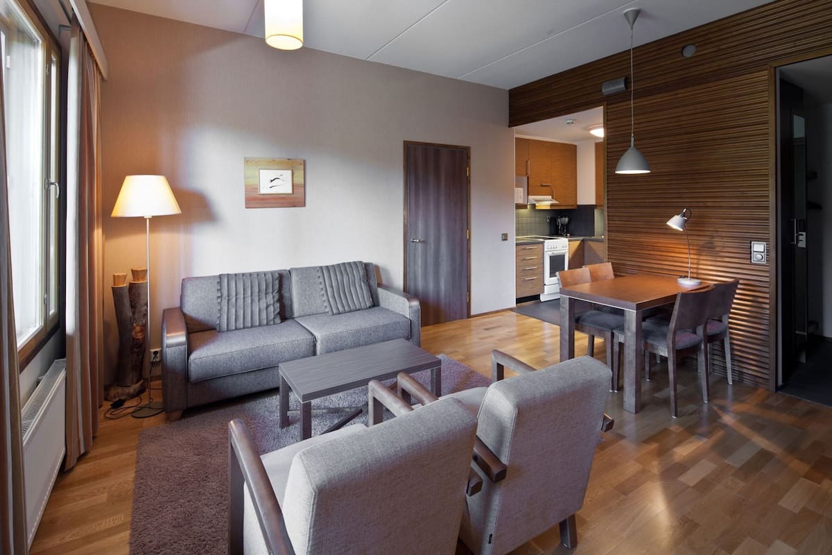 Una sala de estar moderna con sofá, mesa de centro y mesa de comedor con sillas. Se ve un área de cocina a través de una puerta abierta.