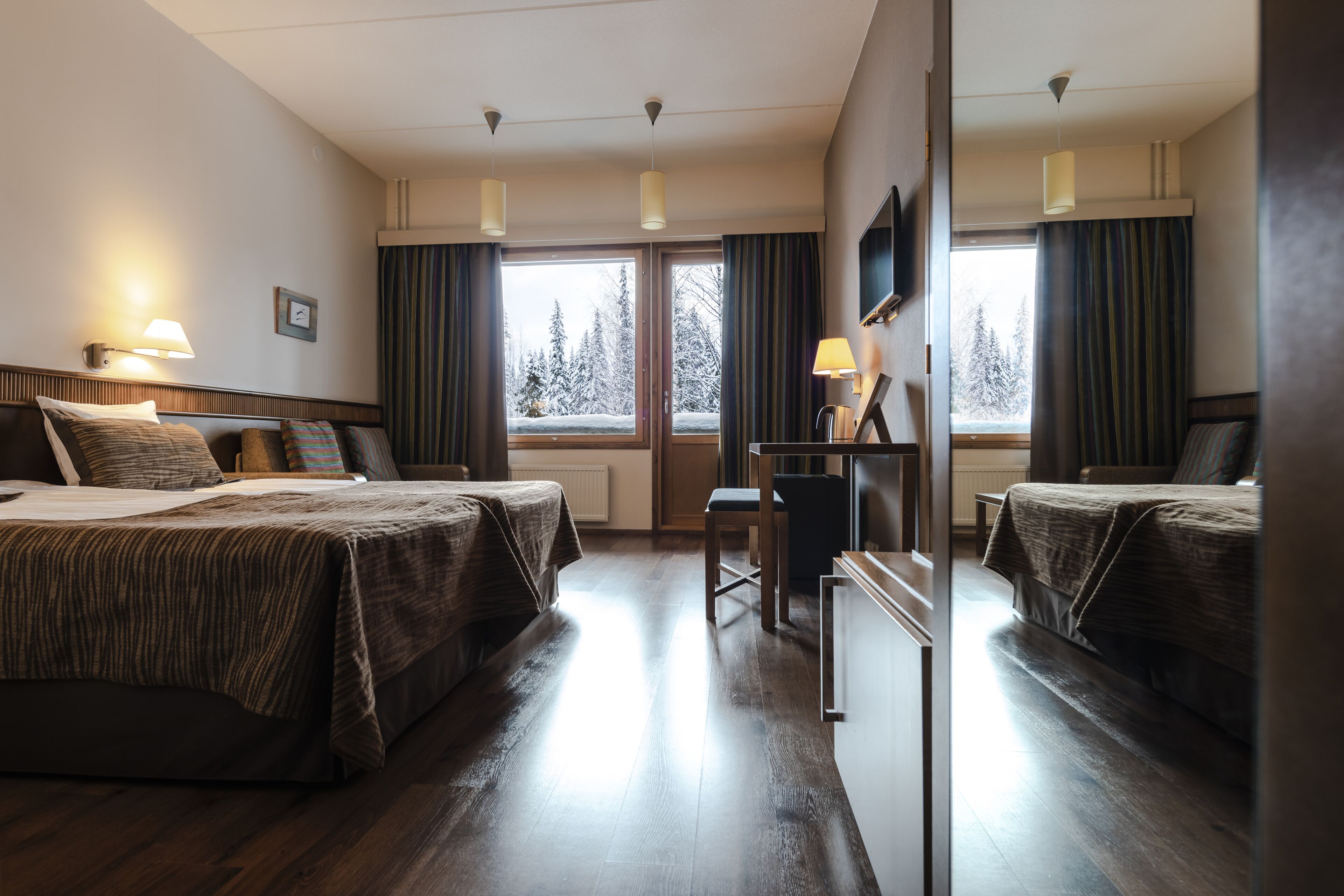 A hotel room with two beds, a desk, and a large window with curtains.