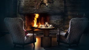 A cozy room with a fireplace, two patterned armchairs, and a round wooden table with glasses and a cup. - Lapland Hotels Luostotunturi (Sodankyla)