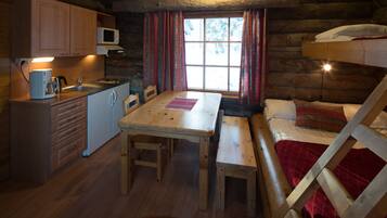 Une cabane chaleureuse avec un intérieur en bois, une table à manger, des bancs, un lit superposé et un coin cuisine équipé d’un four à micro-ondes.