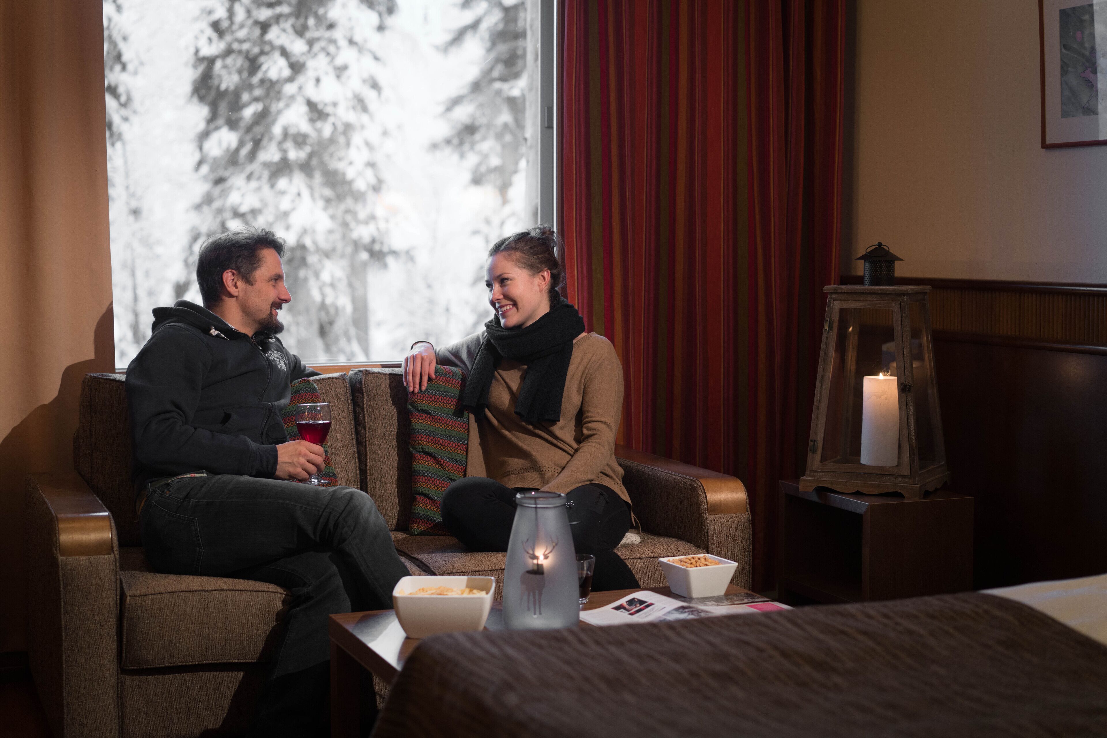 A cozy room with a sofa, a table with snacks, a candle, and a window with a view of trees.