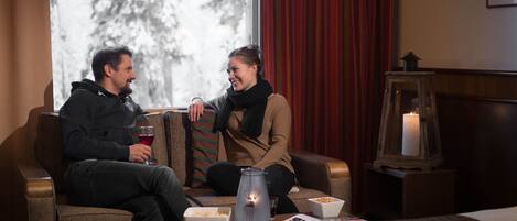 Ein gemütliches Zimmer mit einer Couch, einem Tisch mit Snacks, einer Kerze und einem Fenster mit Blick auf Bäume.