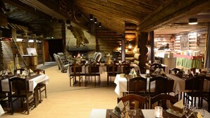 A rustic dining area with wooden tables and chairs, a stone fireplace, and a log wall. - Lapland Hotels Luostotunturi (Sodankyla)