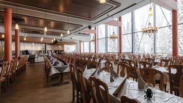 A spacious dining area with long tables and chairs, large windows, and modern lighting fixtures.