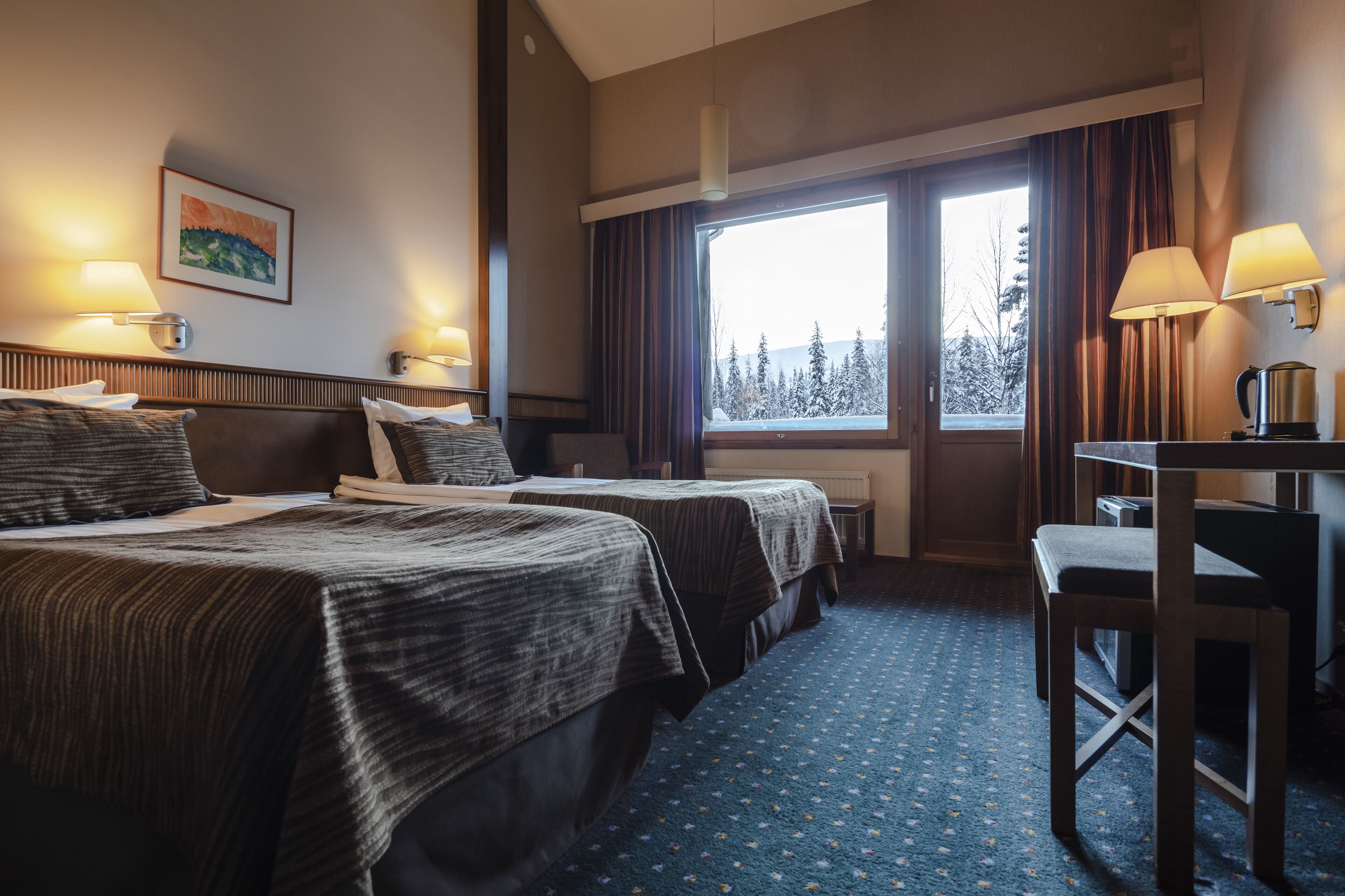 Habitación de hotel con dos camas, un escritorio, una silla, un ventanal con cortinas y un cuadro en la pared.