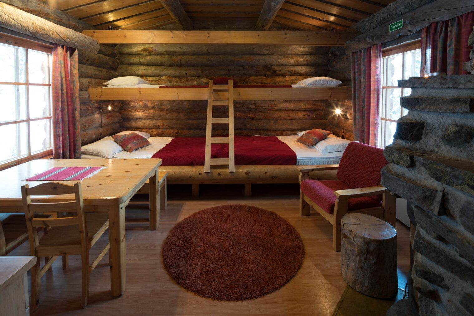 Una habitació d'una cabana de fusta acollidora amb un llit superposat, una taula de fusta amb cadires, una catifa vermella i una paret de pedra.