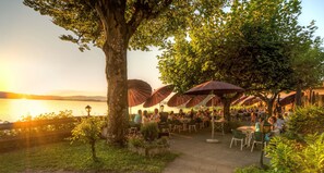 An outdoor dining area with tables and umbrellas, overlooking a body of water. - Seehotel Grauer Bär (Kochel am See)