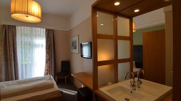 Ein Hotelzimmer mit Bett, Schreibtisch, Fernseher, einem großen Spiegel und einem Badezimmer mit Waschbecken und Spiegel.