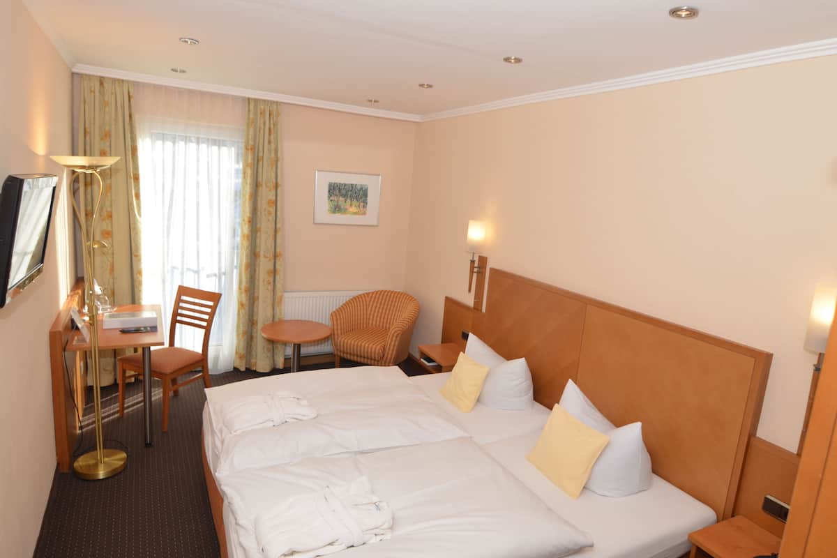 Quarto de hotel com duas camas, uma escrivaninha com cadeira, uma mesinha e uma poltrona.