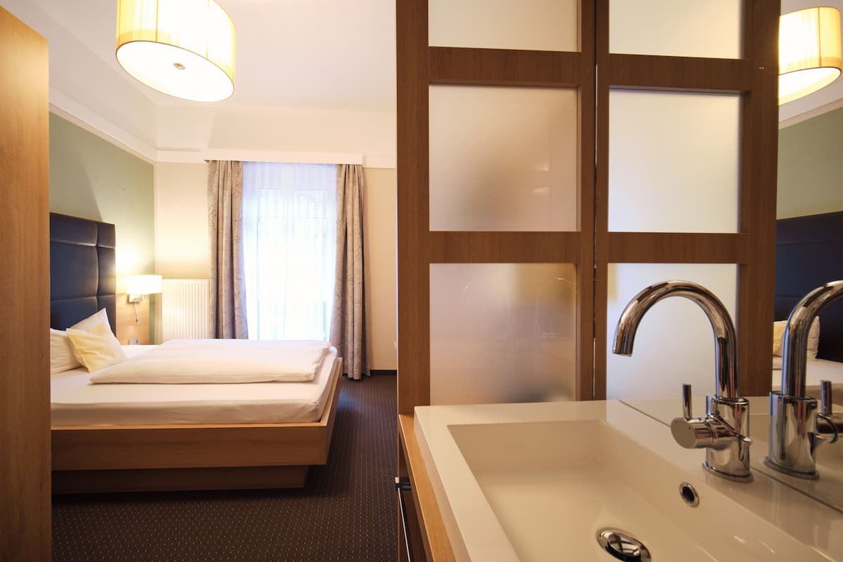 Quarto de hotel com cama, pia grande no banheiro e janela com cortinas.