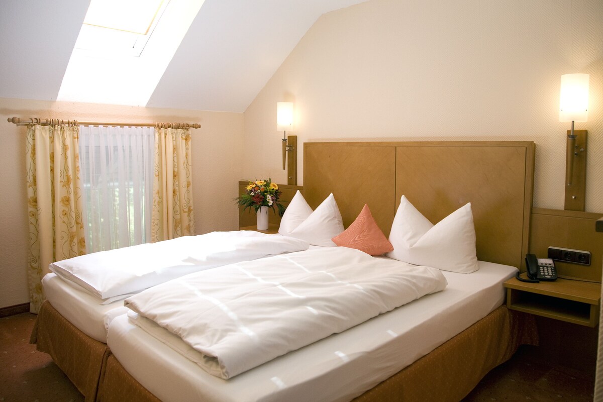 A hotel room with a large bed, a bedside table with a lamp, and a small table with a vase of flowers.