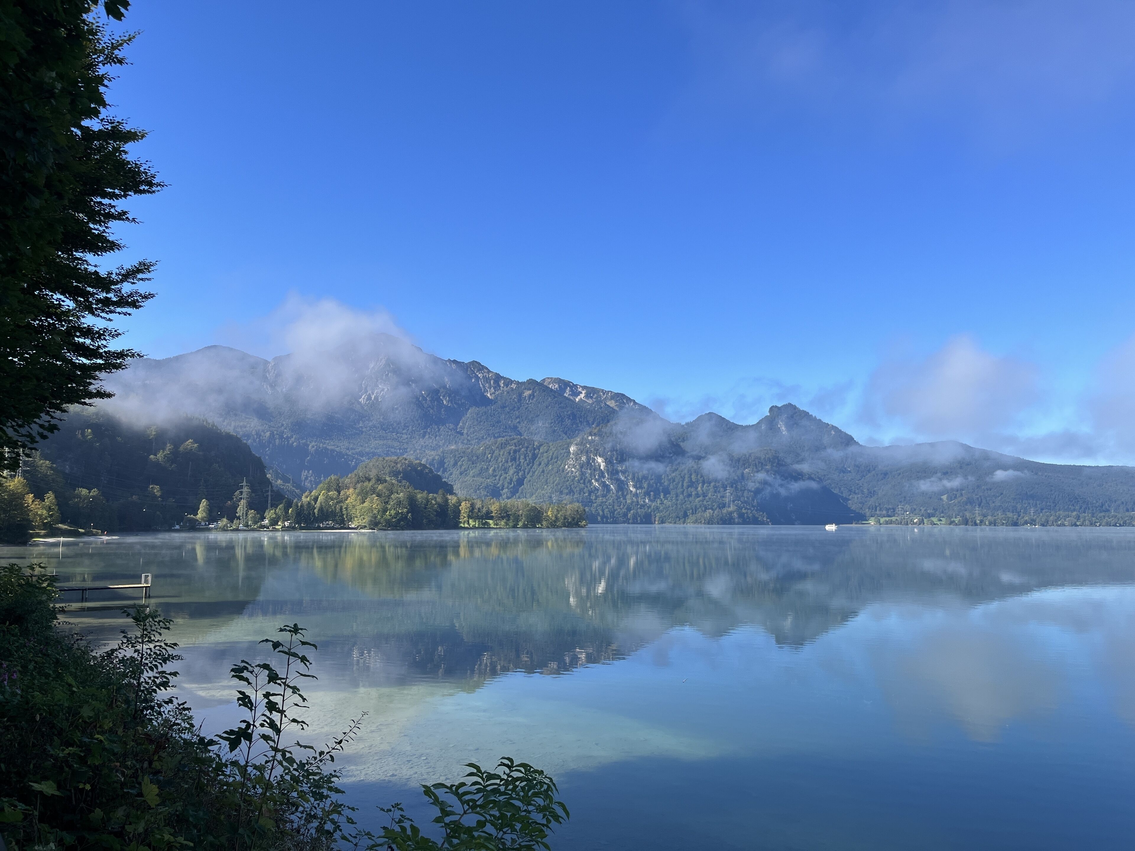 Un lago sereno con reflejos nítidos, rodeado de exuberante vegetación y montañas.