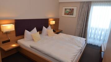 Habitación de hotel con una cama grande, dos mesitas de noche con lámparas, un cabecero, un cuadro en la pared y una ventana con cortinas.