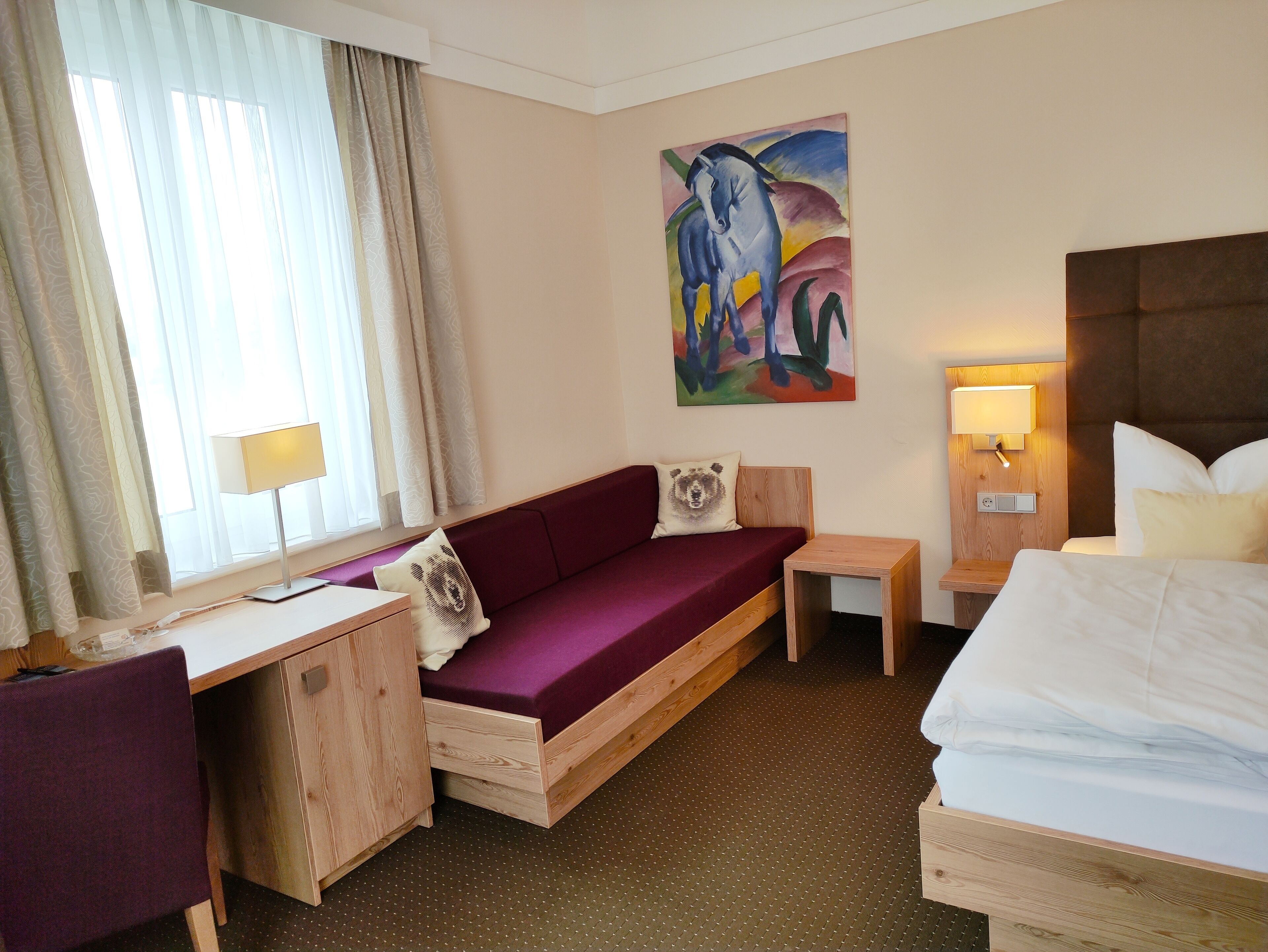 A hotel room with a wooden desk, purple sofa, and a bed.