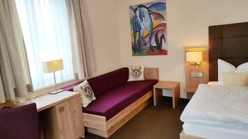 A hotel room with a wooden desk, purple sofa, and a bed.