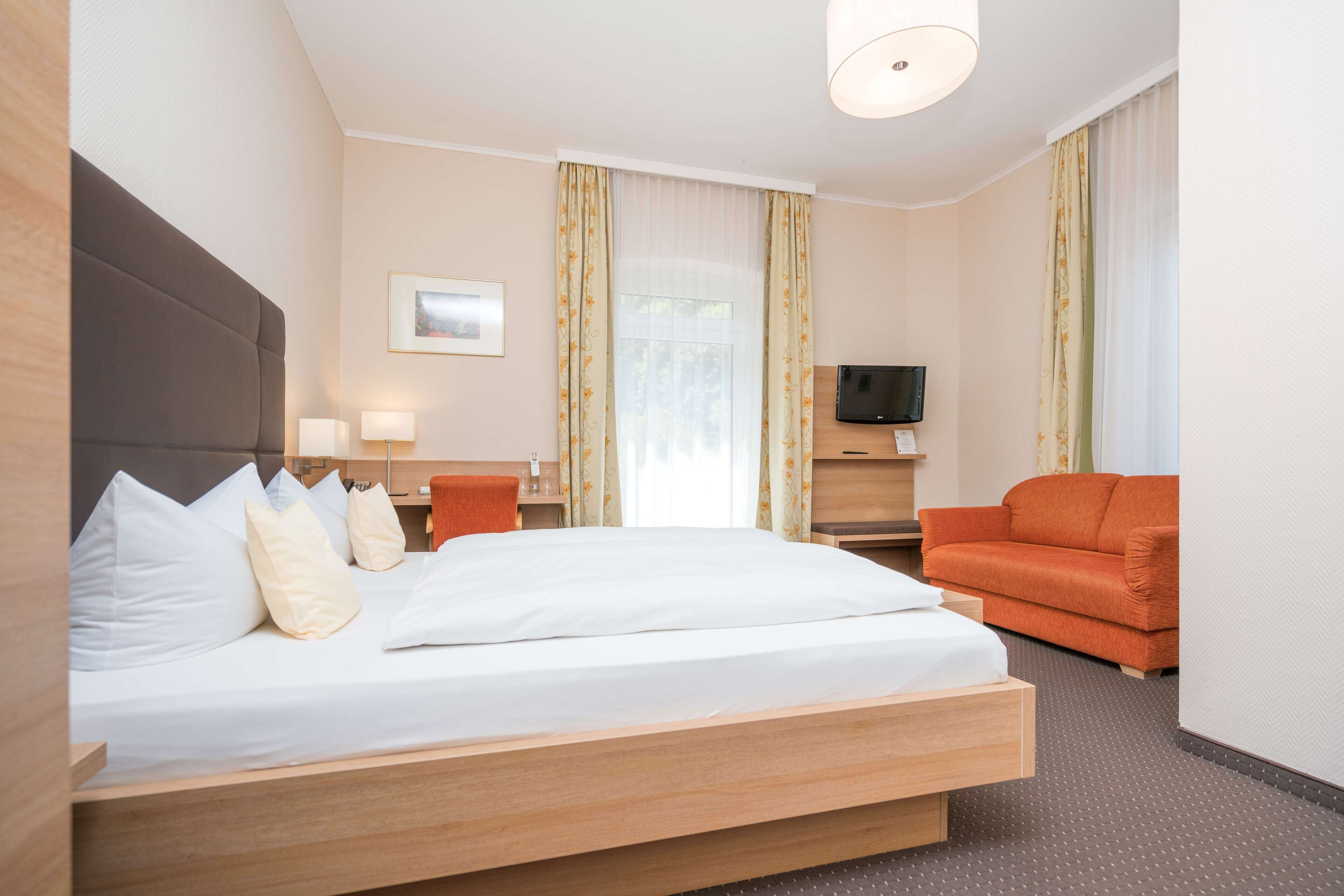 Quarto de hotel com cama, sofá, televisão e janela com cortinas.