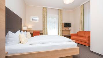 Quarto de hotel com cama, sofá, televisão e janela com cortinas.