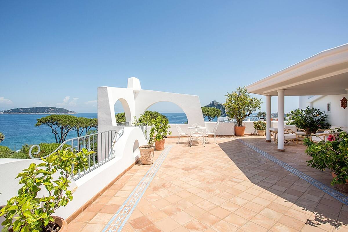 Eine Terrasse mit Meerblick, weißen architektonischen Elementen und Sitzmöbeln im Freien.