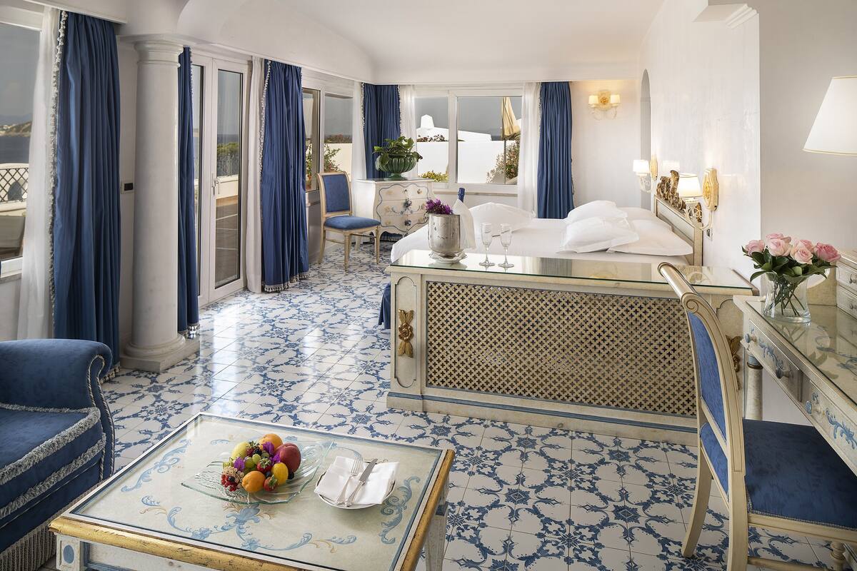 Ein Hotelzimmer mit Balkon, einem Essbereich mit Tisch für zwei Personen und einem Bett mit Nachttisch.
